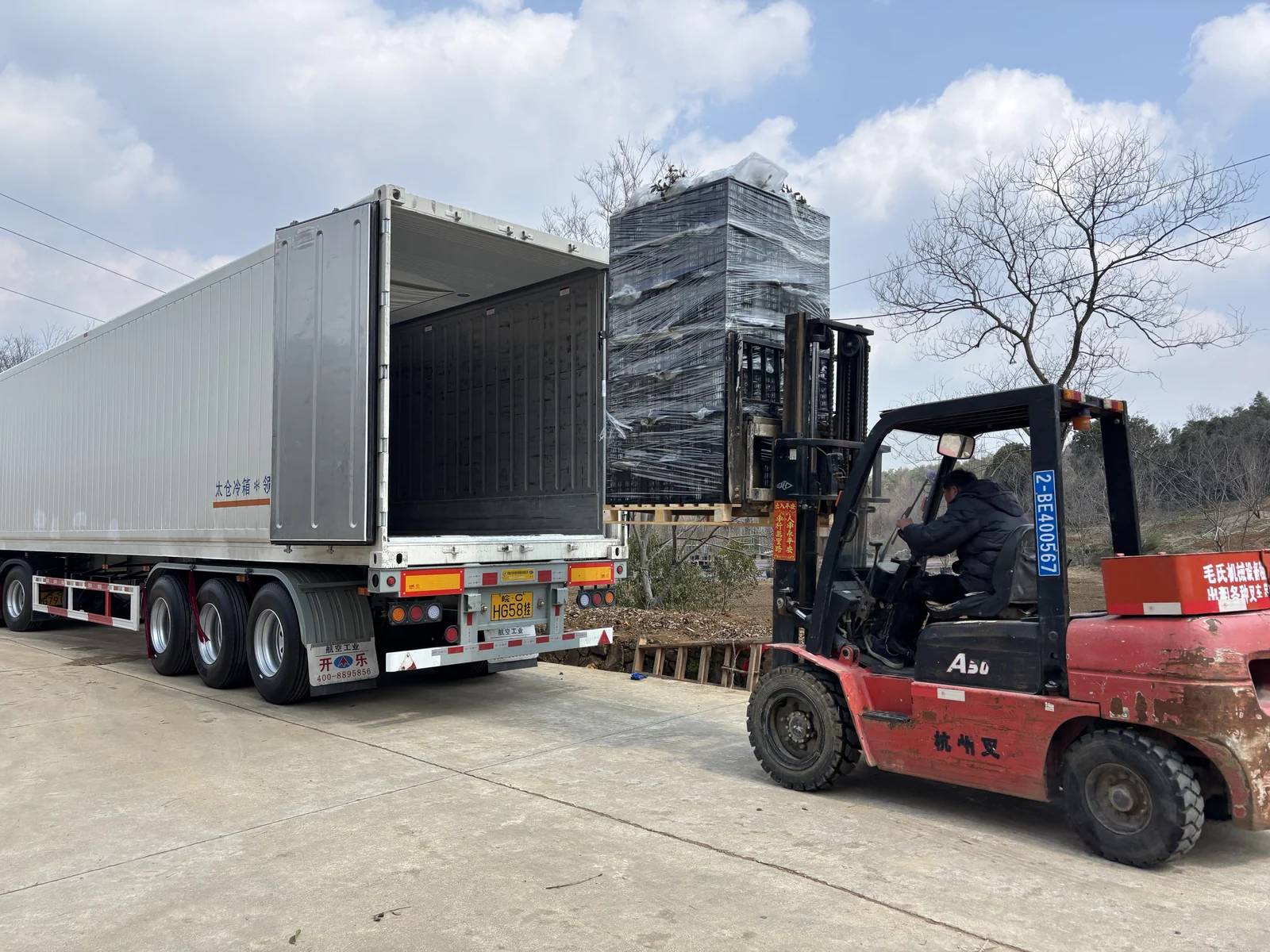 A forklift positions a stretch-wrapped pallet at the container entrance.